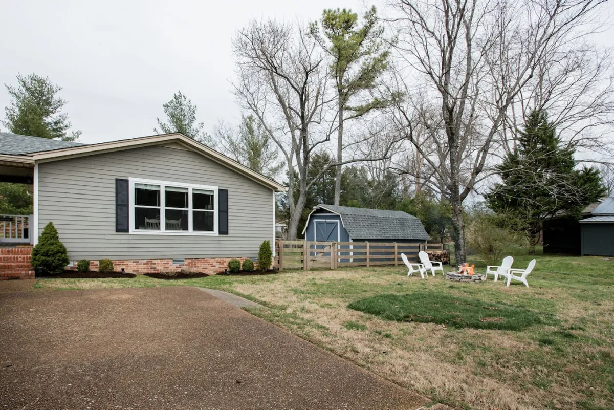 This exterior image features the home's facade with a welcoming lawn area, a fire pit surrounded by seating, and a shed in the background. The photo captures a spacious outdoor setting perfect for gatherings and play, with ample green space inviting children to explore and families to relax together.