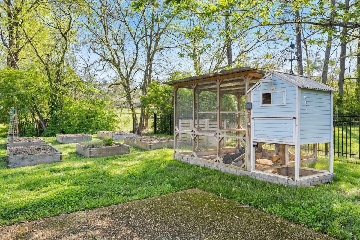 An exterior shot featuring a chicken coop, raised garden beds, and lush greenery. The scene is peaceful and inviting, suggesting activities like gathering farm-fresh eggs and harvesting from the garden just steps from the kitchen.