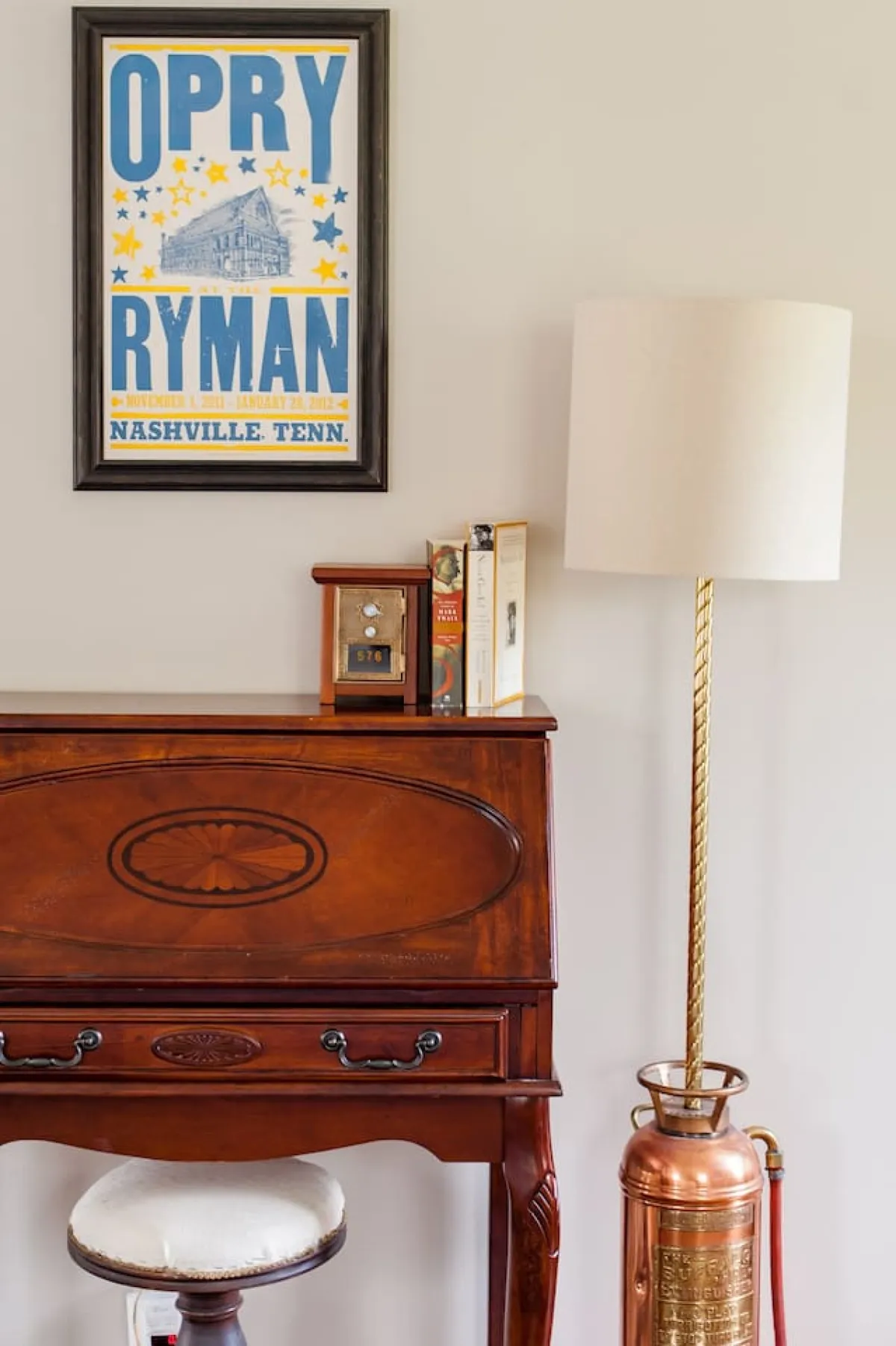 A cozy study nook featuring a wooden desk with books, a vintage-style lamp, and a prominent Opry Ryman poster on the wall, evoking Nashville’s musical heritage. The decor includes a vintage clock and touches that invite relaxation and storytelling.